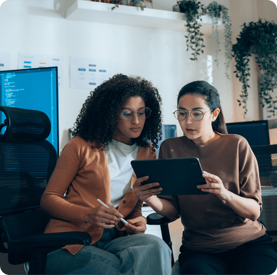 Two people sitting in office chairs, looking at a tablet together in a workspace. This keeps it short, clear, and accessible while highlighting the collaborative action. Would you like me to also create a slightly longer version that emphasizes teamwork and data review for business or SEO contexts?