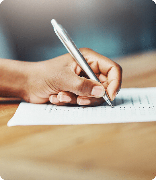 A close‑up of a hand holding a silver pen and filling in circles on a multiple‑choice test sheet placed on a wooden surface.